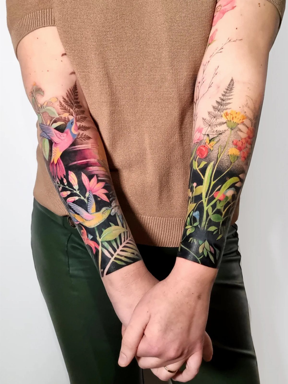 Colorful illustrative tattoos of birds and tropical plants on a person's forearms.