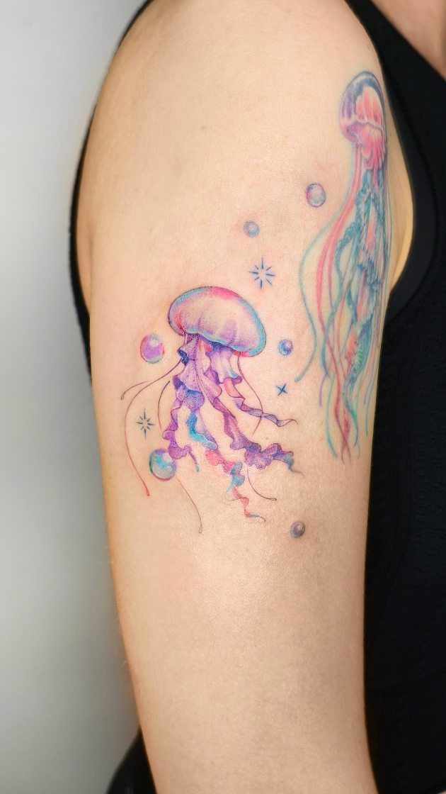 Pastel jellyfish tattoos with soft pink and purple hues on an upper arm.