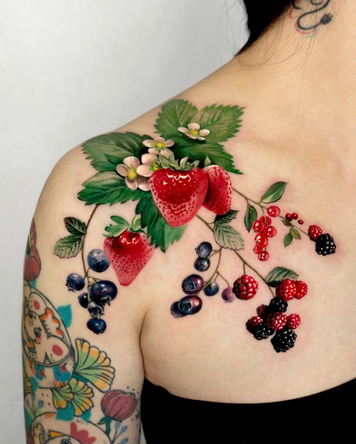 Realistic tattoo of strawberries, blueberries, and blackberries on a person's shoulder