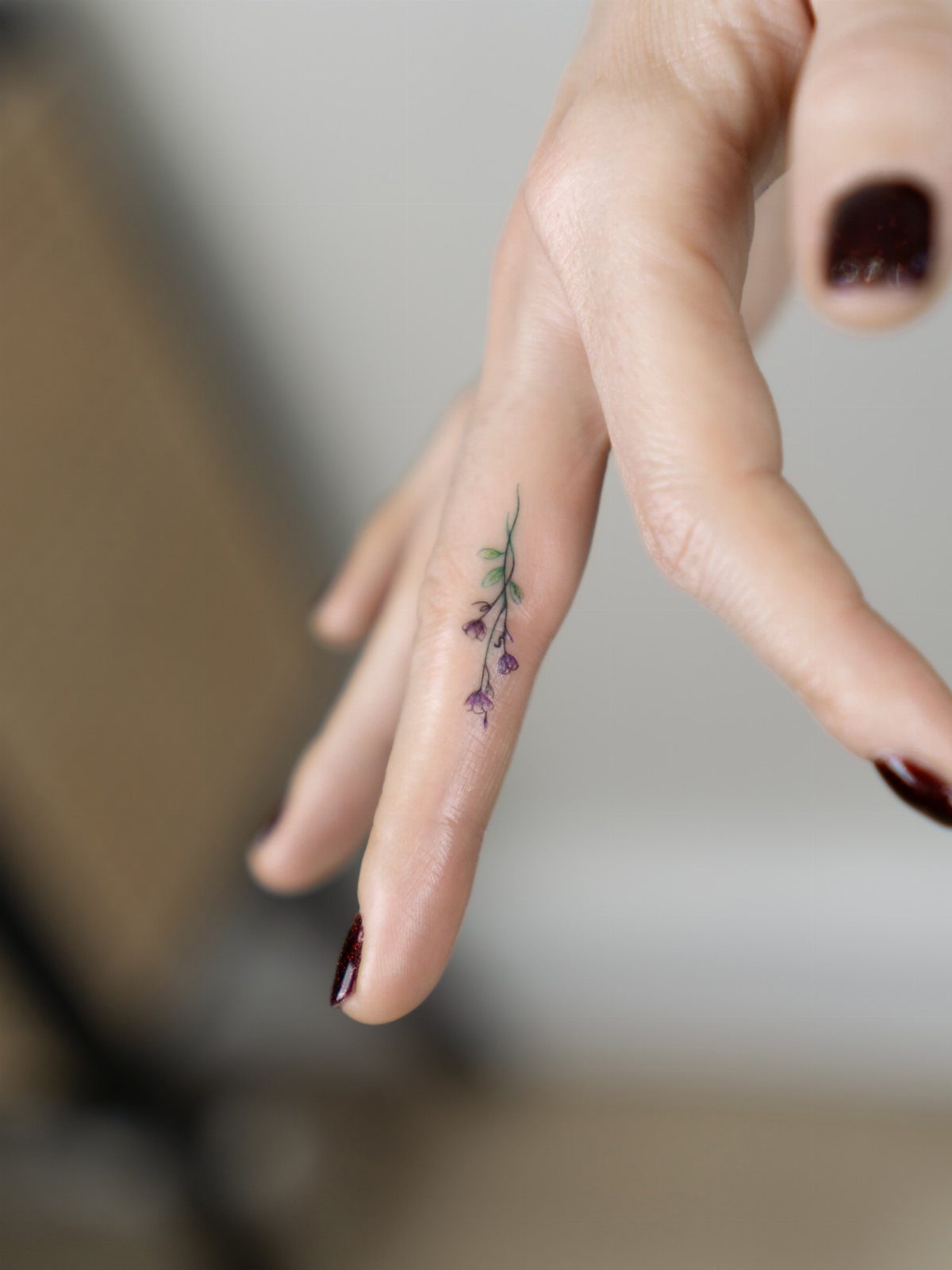 Small purple flower tattoo with green leaves on a person's index finger.