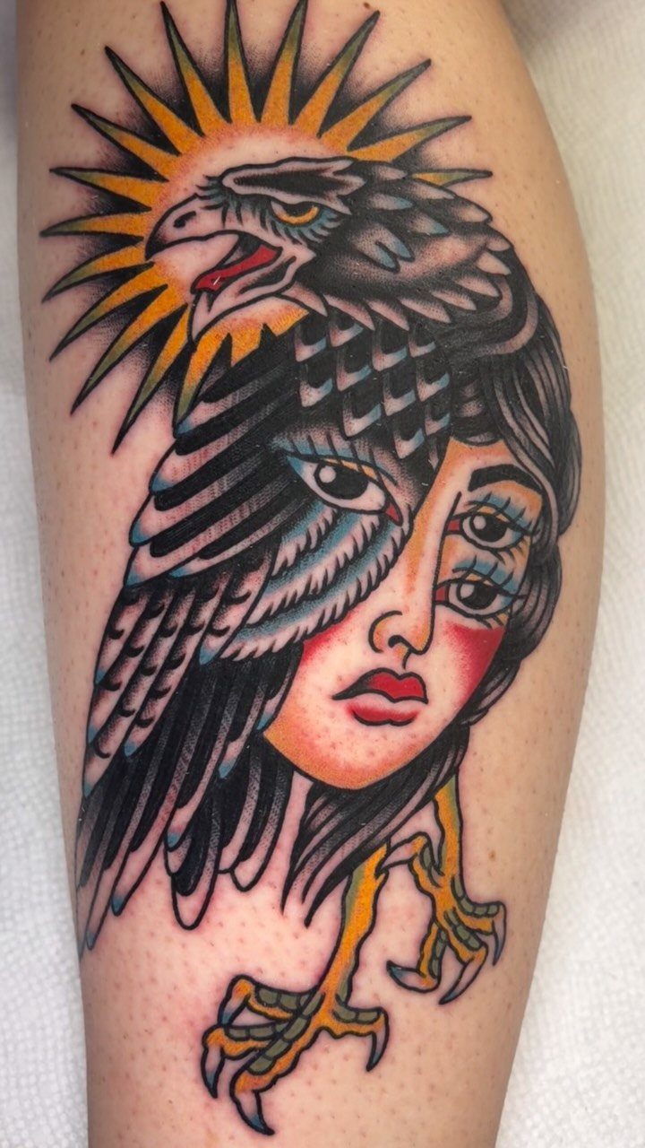 Surreal tattoo of a woman's face merged with a black eagle and sunburst.