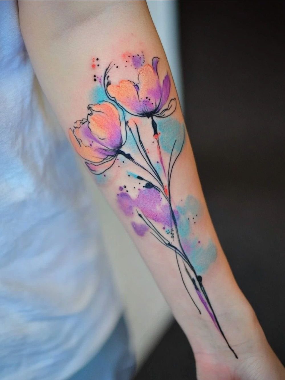 Watercolor style tattoo of two colorful flowers on a person's forearm.