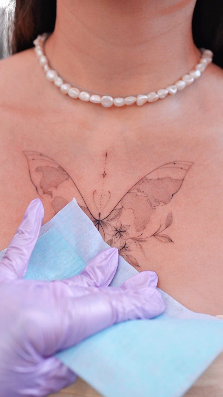 Butterfly tattoo with floral accents on a chest being wiped by a gloved hand.