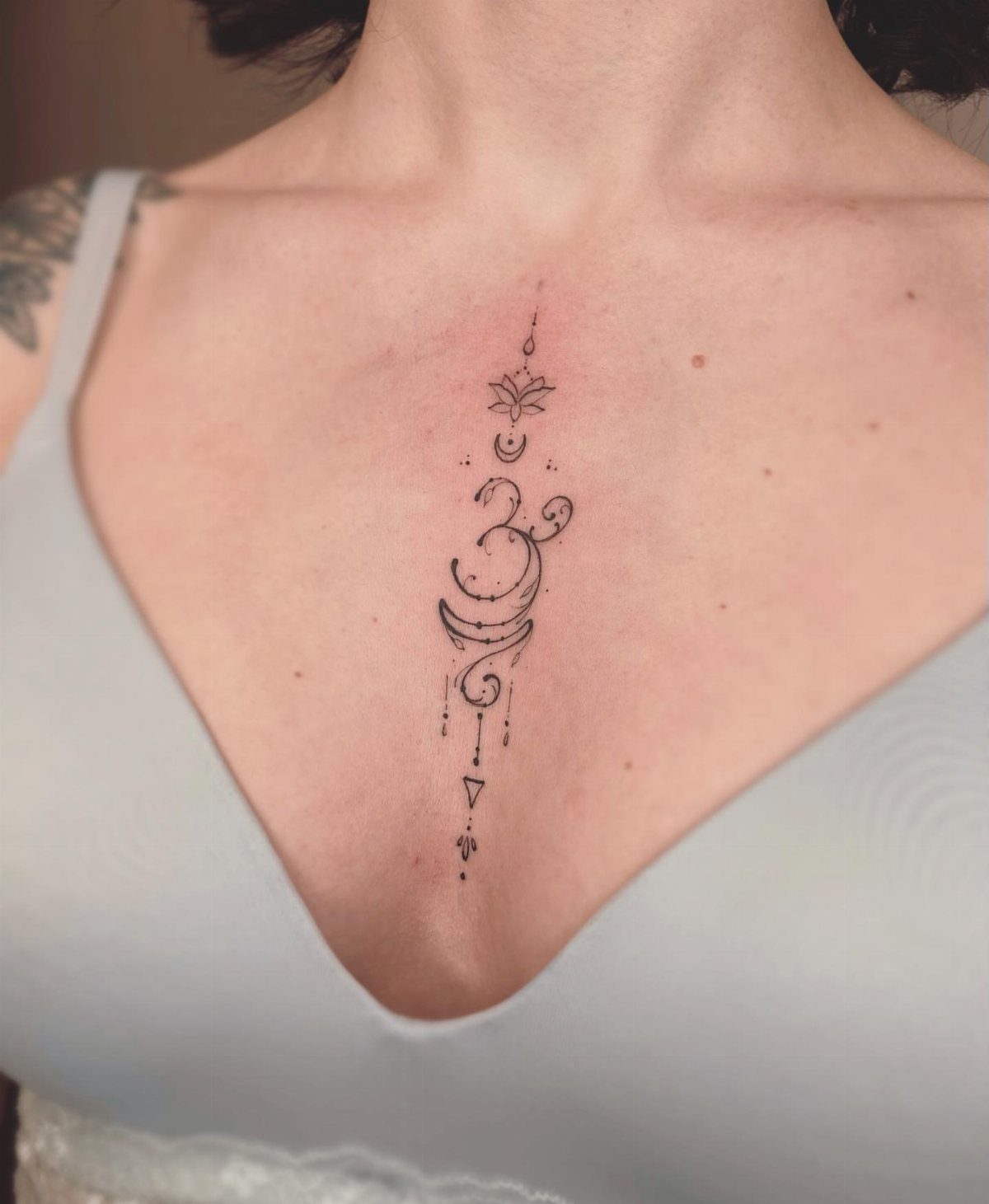 Vertical chest tattoo featuring a small lotus flower, Om symbol, and crescent moon.