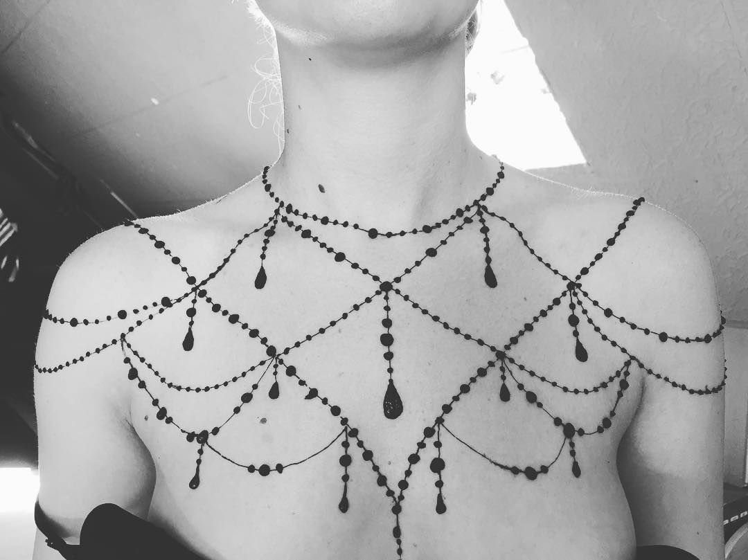 Intricate chandelier-style henna tattoo on a person's chest and shoulders in black and white.