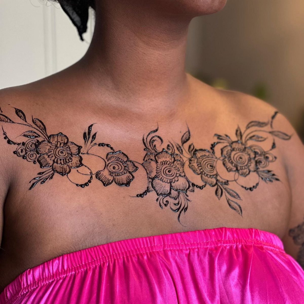 Chest henna tattoo featuring symmetrical floral patterns and swirling vines on a person.