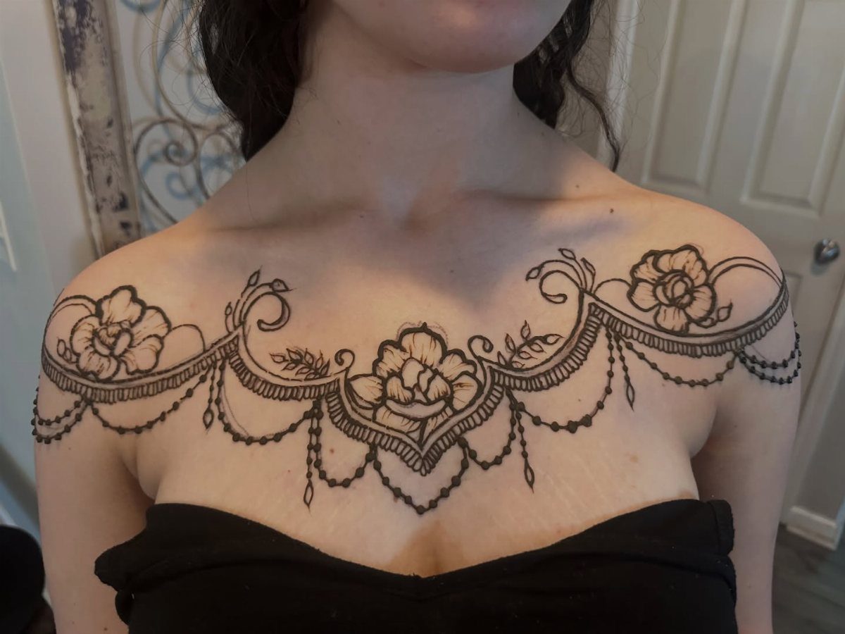 Henna tattoo on a chest featuring symmetrical roses and draped bead patterns.