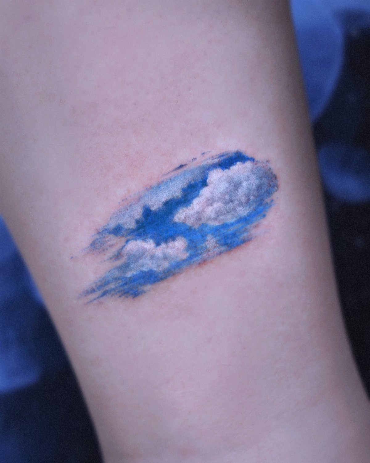 Tattoo of a blue sky with white clouds on a person's arm