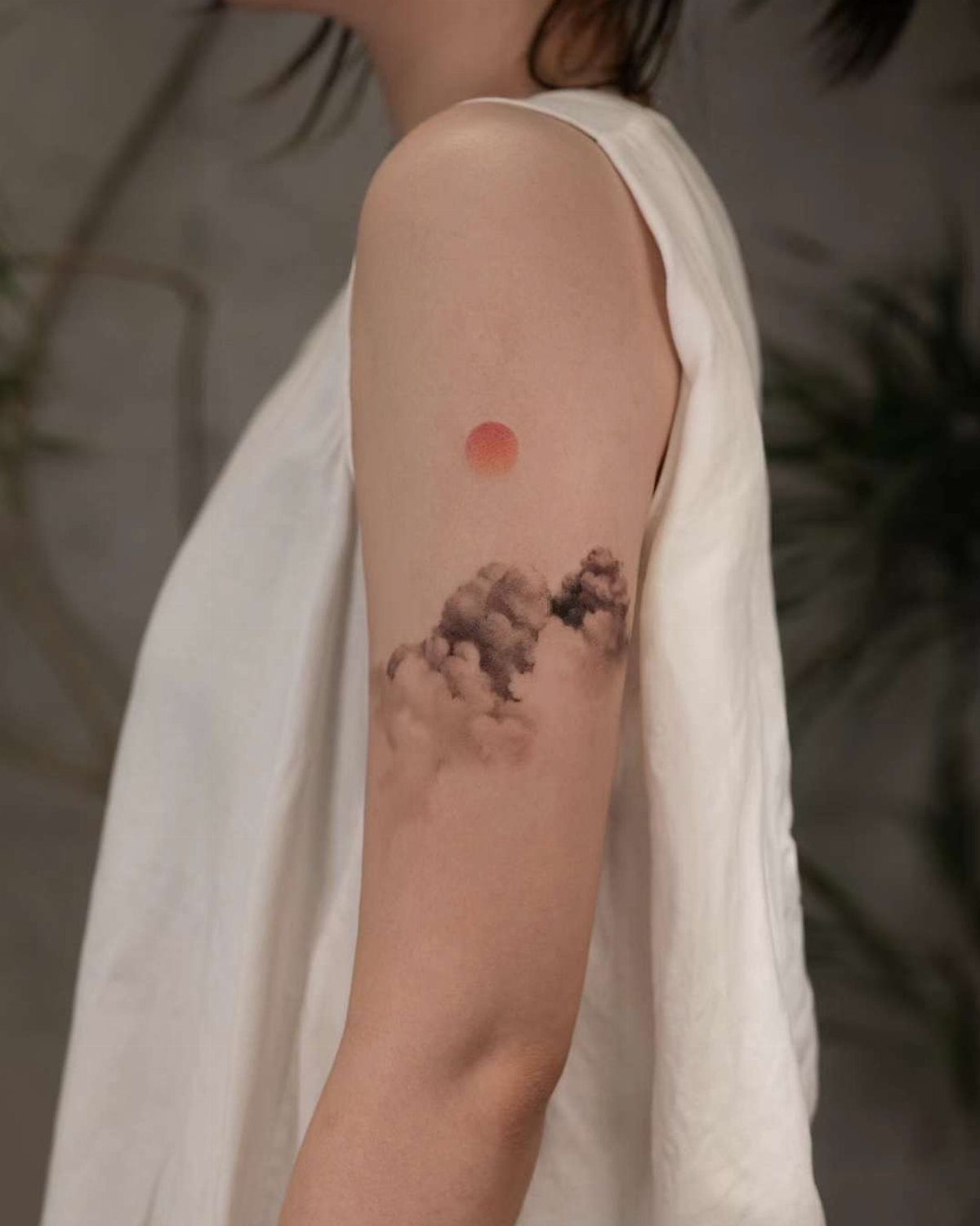Tattoo of grey clouds and a red sun on a person's upper arm