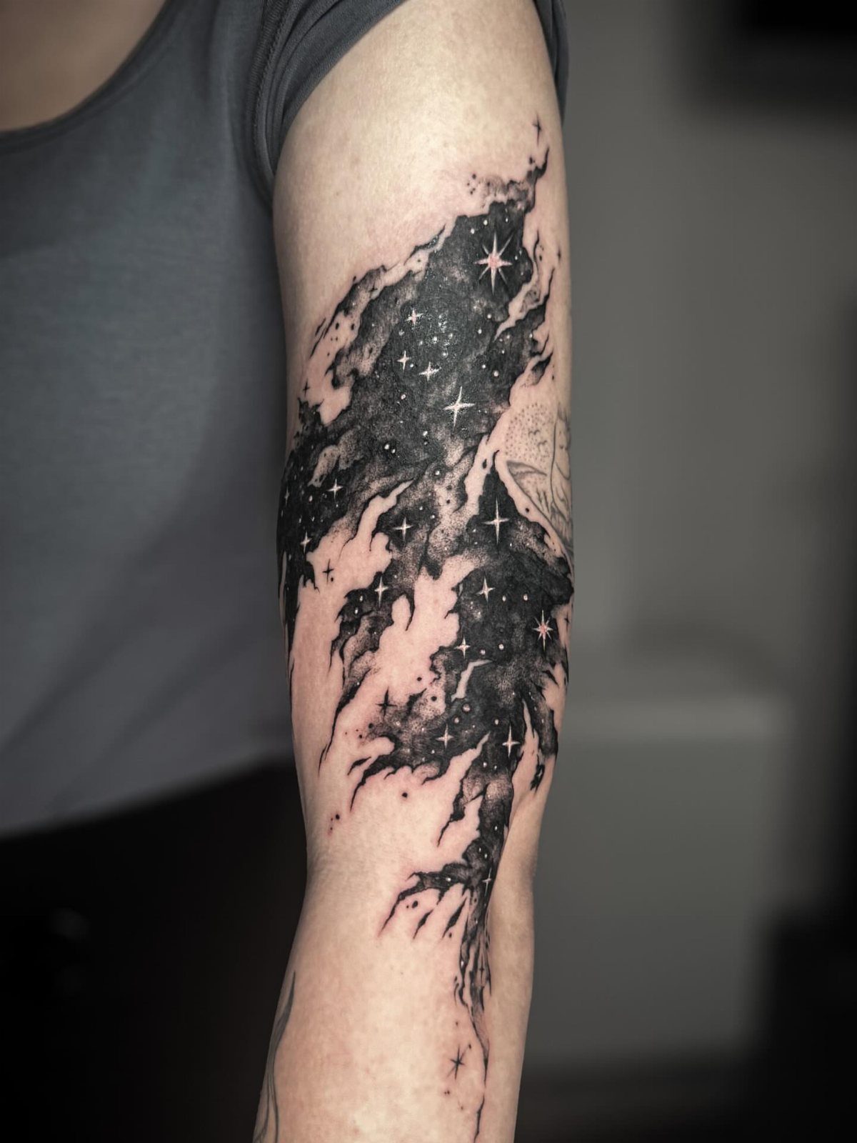 Black and grey cloud tattoo with stars on a person's upper arm