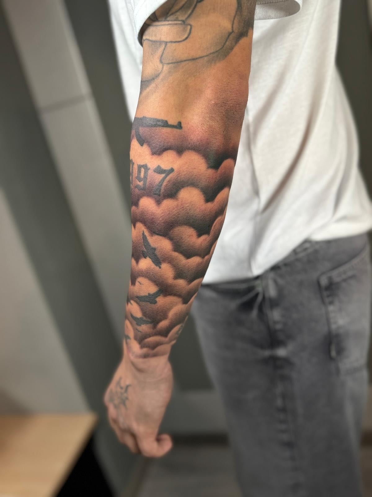 Forearm tattoo featuring dense black and grey billowing clouds with integrated aircraft silhouettes.