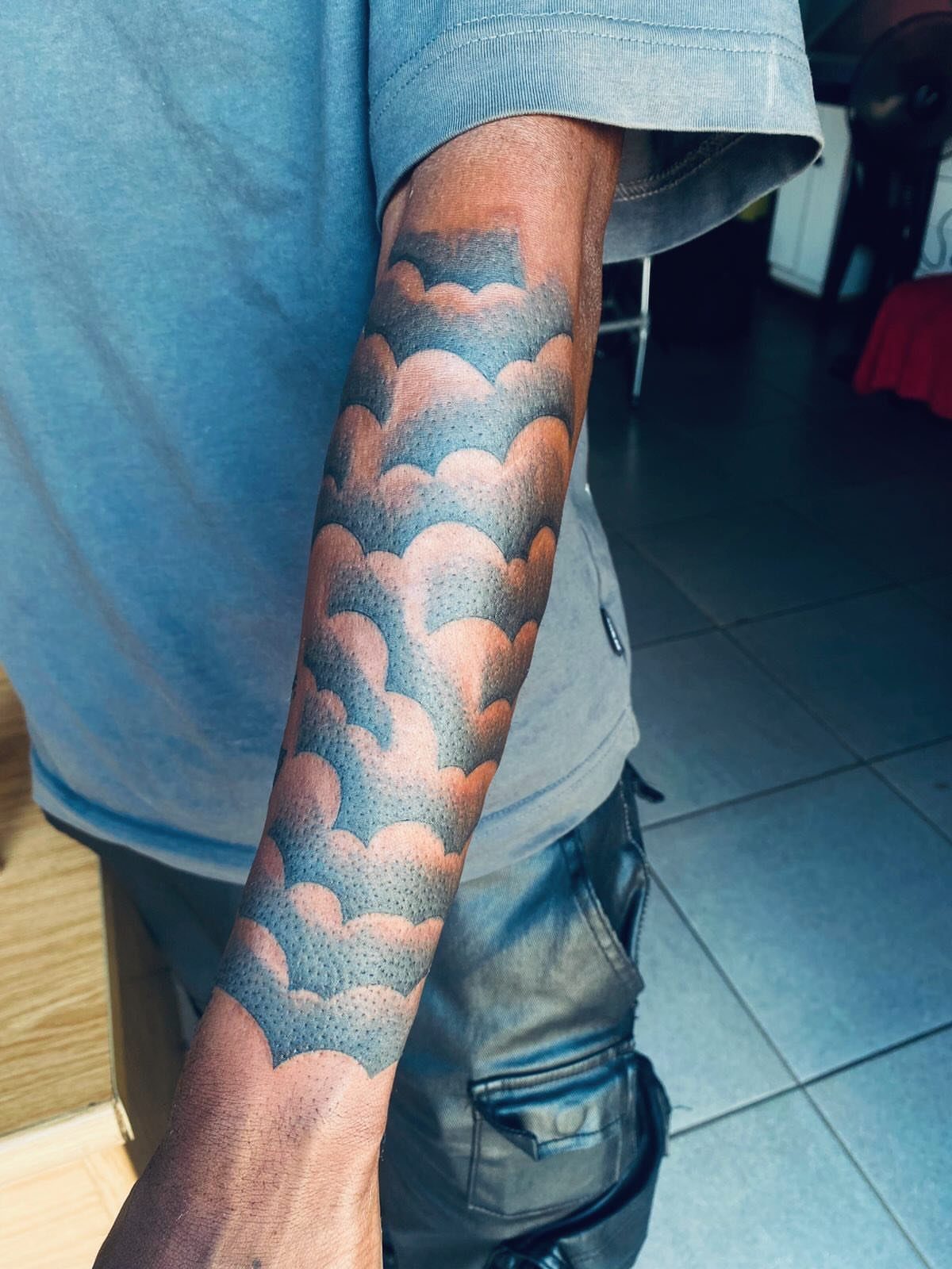 Layered fluffy cloud tattoo filler with stippled shading on a person's forearm