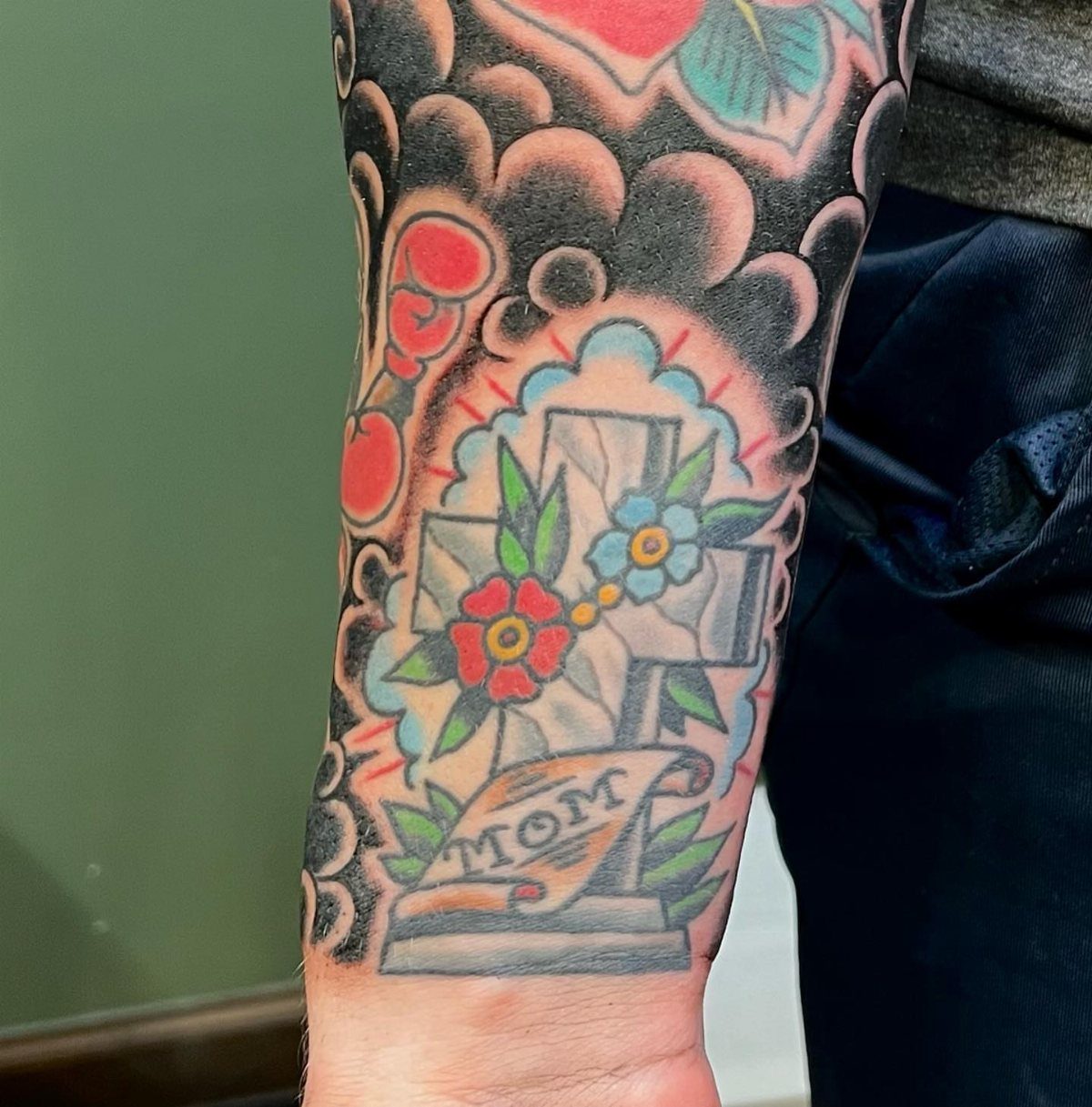Traditional tattoo on a forearm featuring a cross surrounded by bold swirling cloud filler.