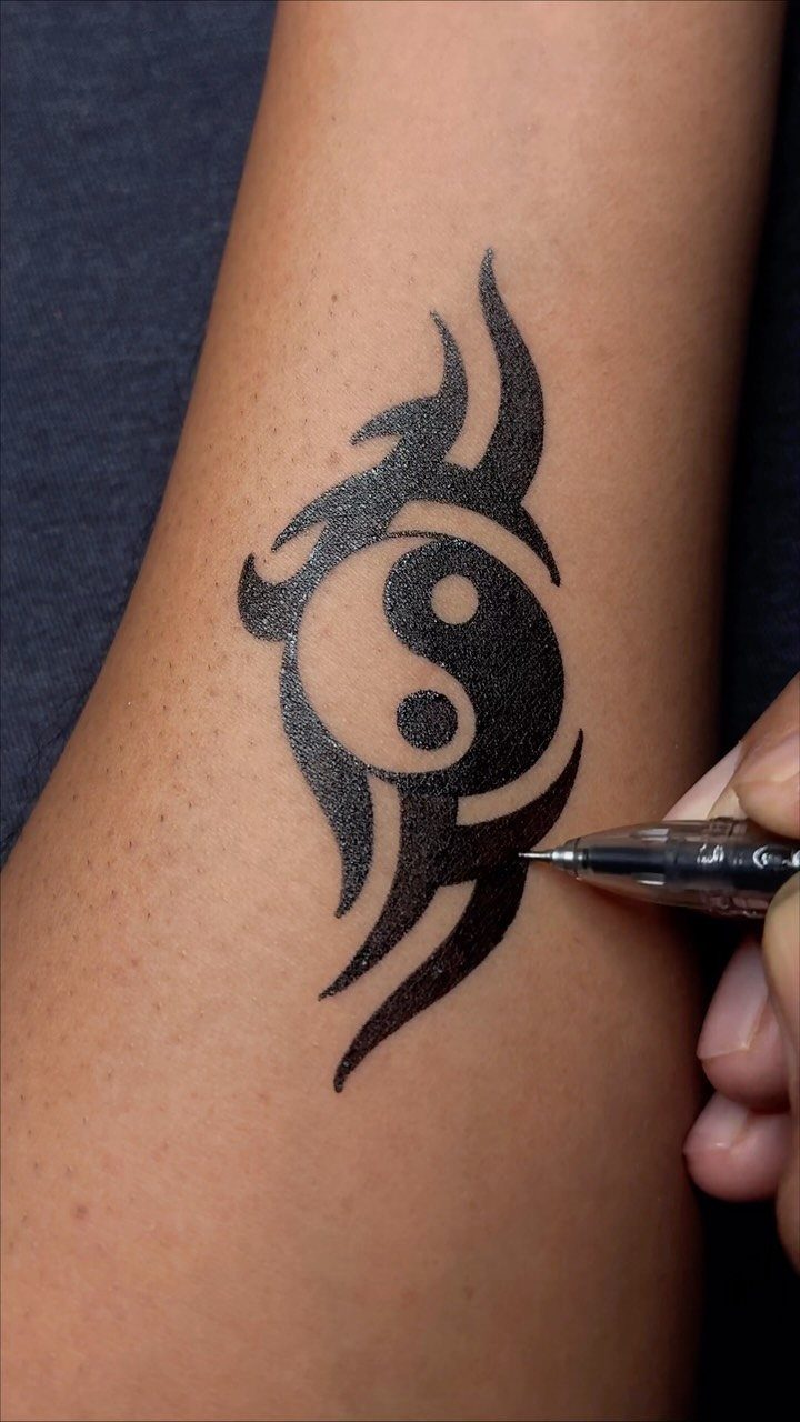 Black ink pen tribal yin-yang design being drawn on a person's forearm.