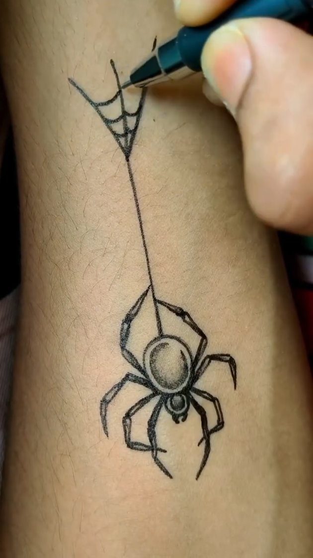 Black ink pen drawing of a spider hanging from a web on a forearm