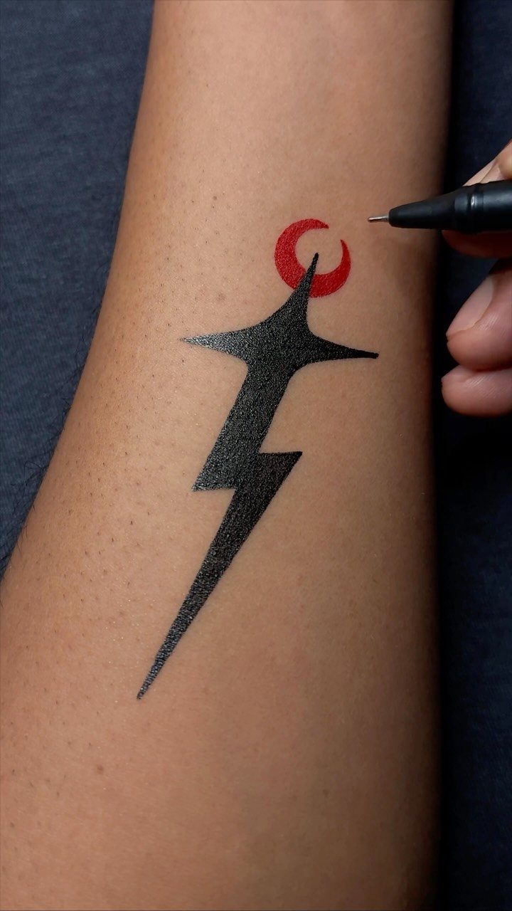 Stylized black ink lightning bolt and red crescent moon drawn on a forearm