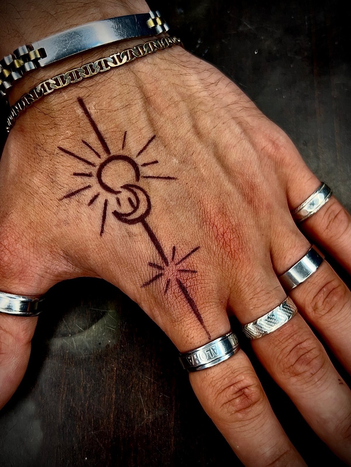 Hand with black ink pen drawings of a sun and crescent moon symbol.