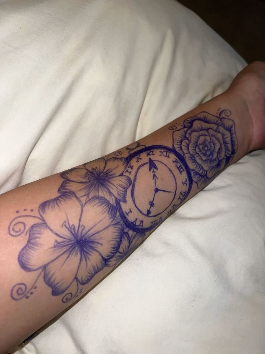 Blue ink pen drawings of flowers and a clock on a forearm