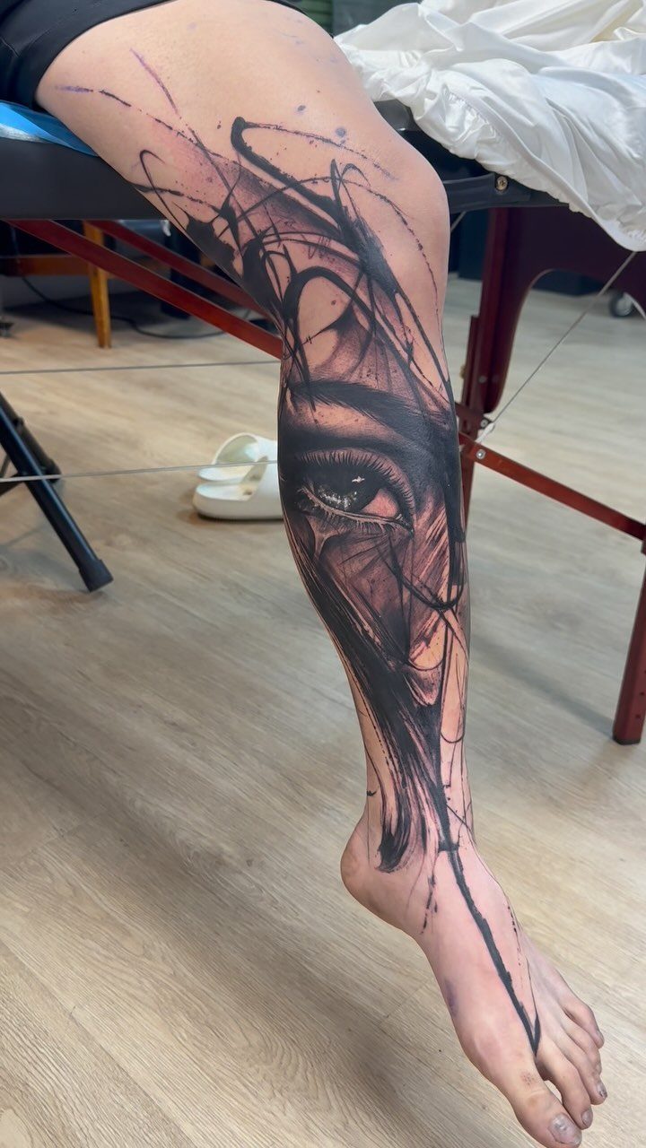 Abstract black ink tattoo of an eye and scribbled lines on a leg.