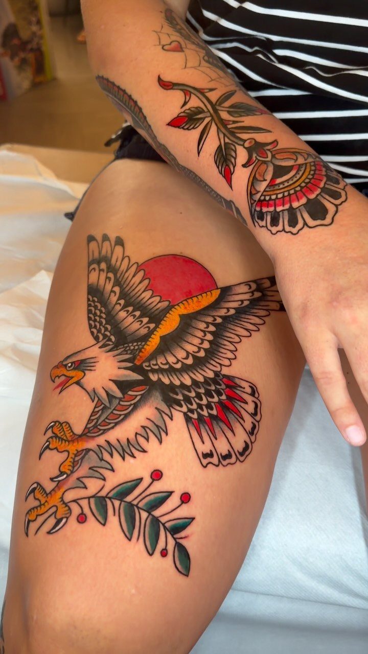 Eagle tattoo with a red sun on a person's thigh in traditional style.