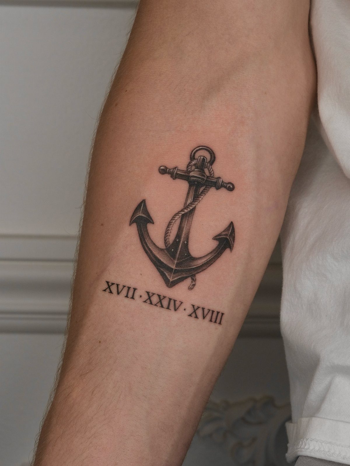 Anchor tattoo entwined with rope and Roman numerals on a person's forearm.