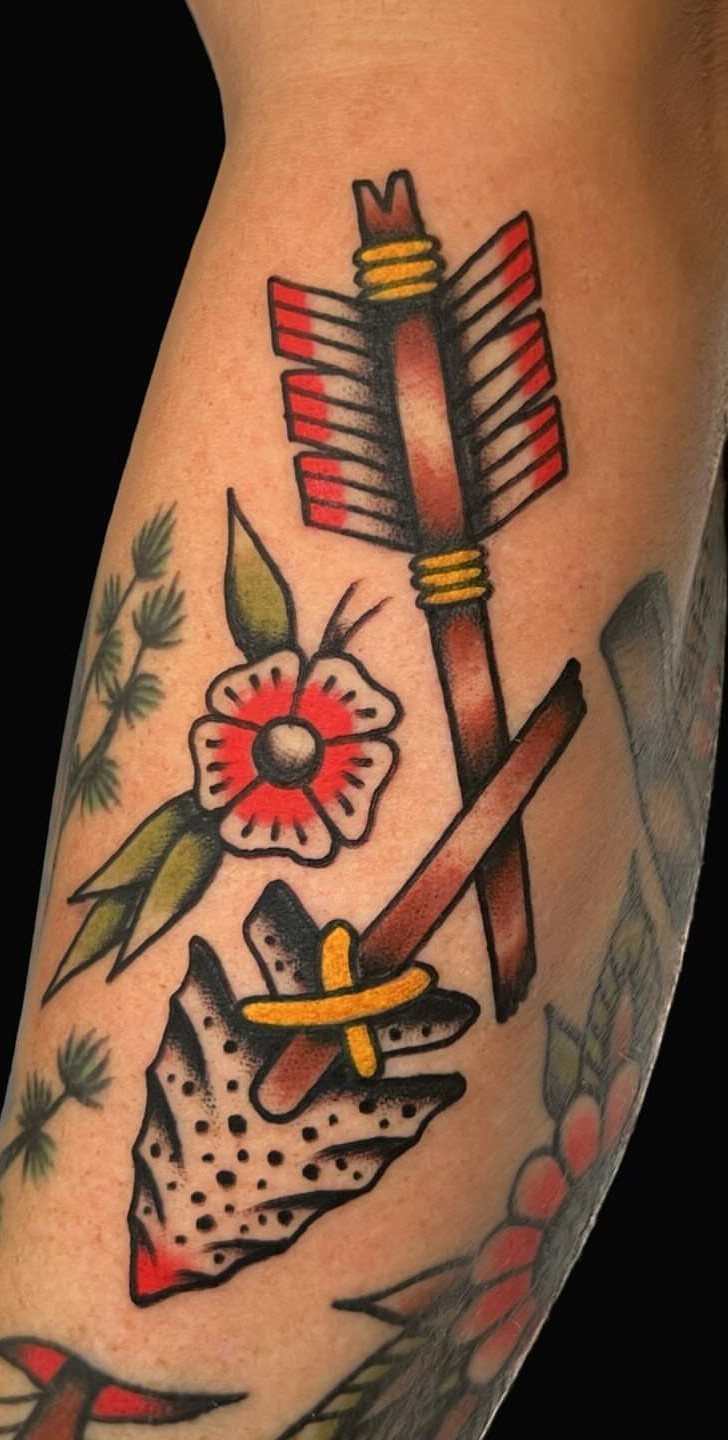 Traditional style tattoo of a brown arrow and red flower on an arm.