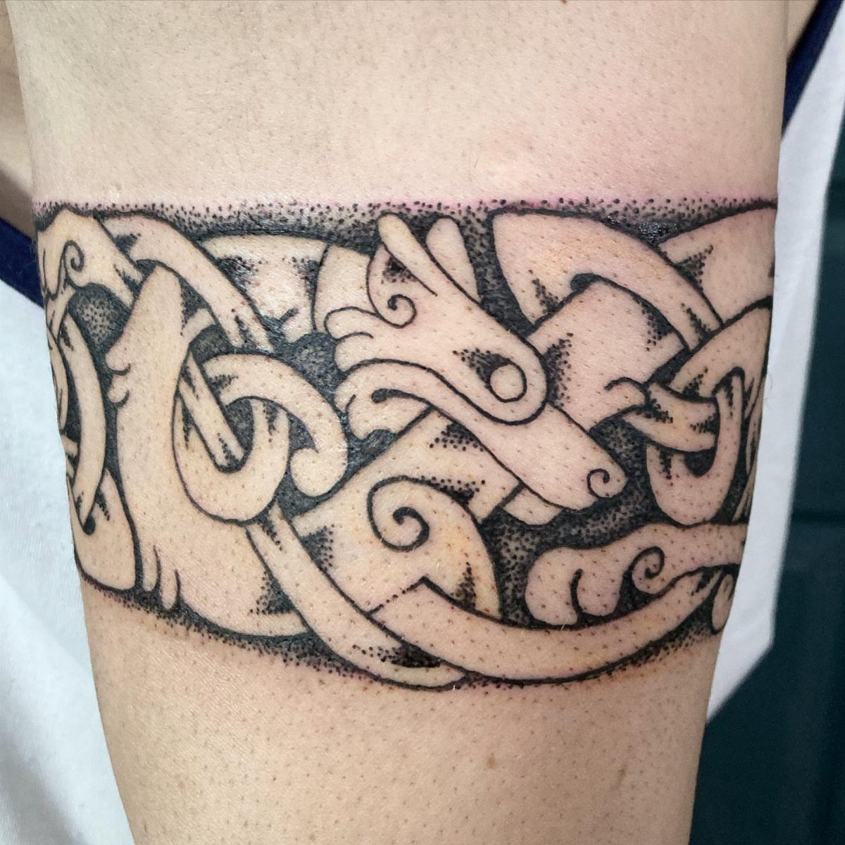 Celtic knotwork tattoo band on an arm featuring interlocking patterns and stylized animals.
