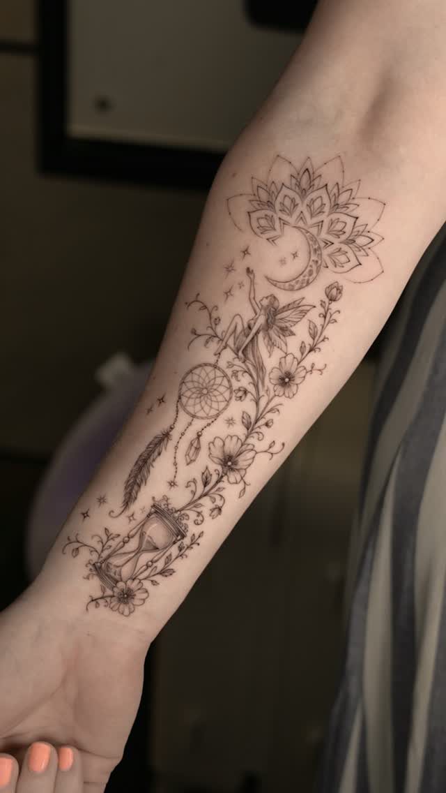 Forearm tattoo featuring a dreamcatcher, fairy, crescent moon, and hourglass with floral accents.