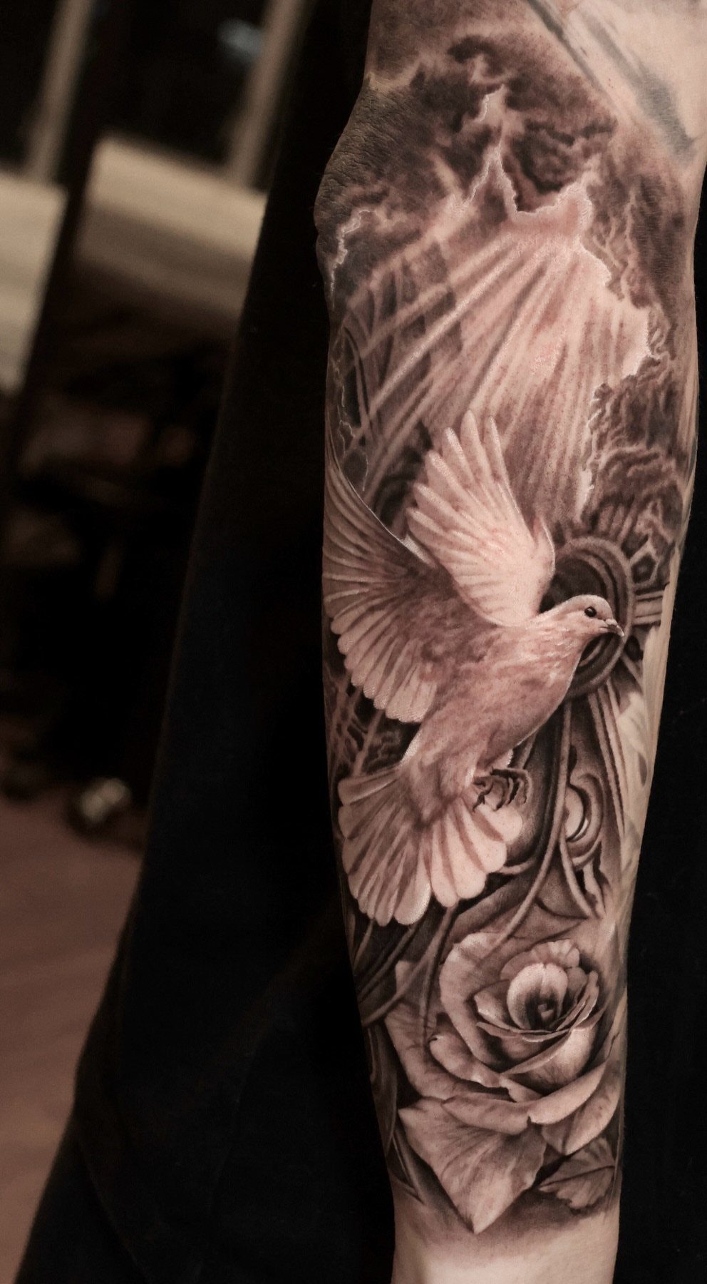 Flying dove and rose tattoo in black and grey realism on a forearm.