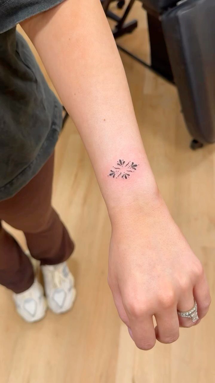 Small black minimalist tattoo of four symmetrical symbols on a person's inner wrist.