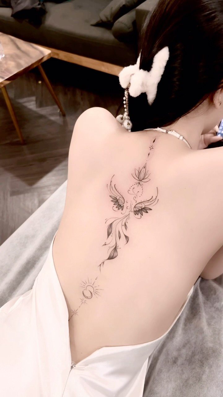 Stylized phoenix tattoo with a moon and sun on a woman's back.
