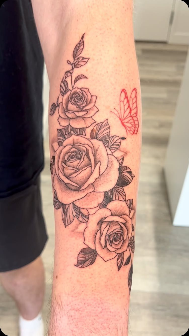 Forearm tattoo of three shaded roses and a small red outline butterfly.