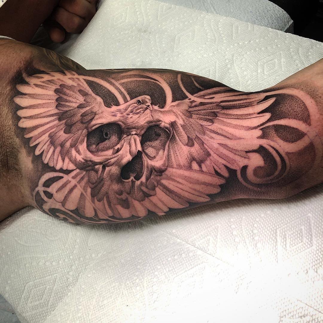 Flying dove tattoo superimposed over a human skull on a person's forearm.