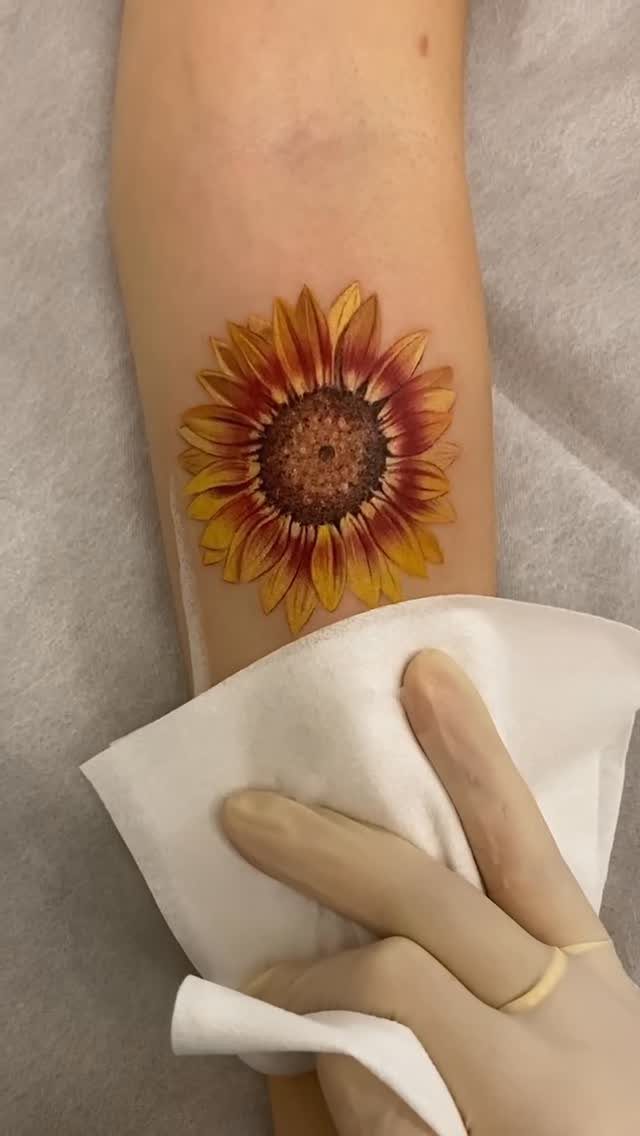 Sunflower tattoo on a forearm being wiped with a white paper towel.