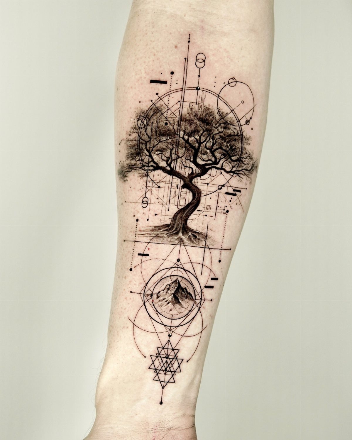 Tree of life tattoo with geometric patterns and a mountain on a forearm.