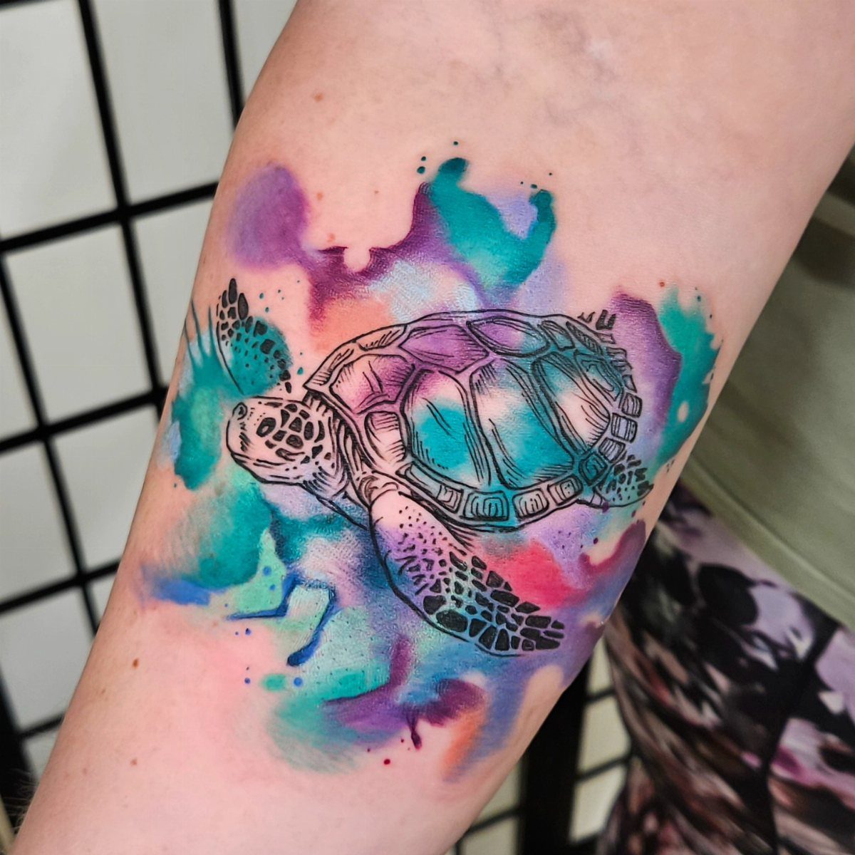 Sea turtle tattoo with vibrant purple and blue watercolor splashes on an arm