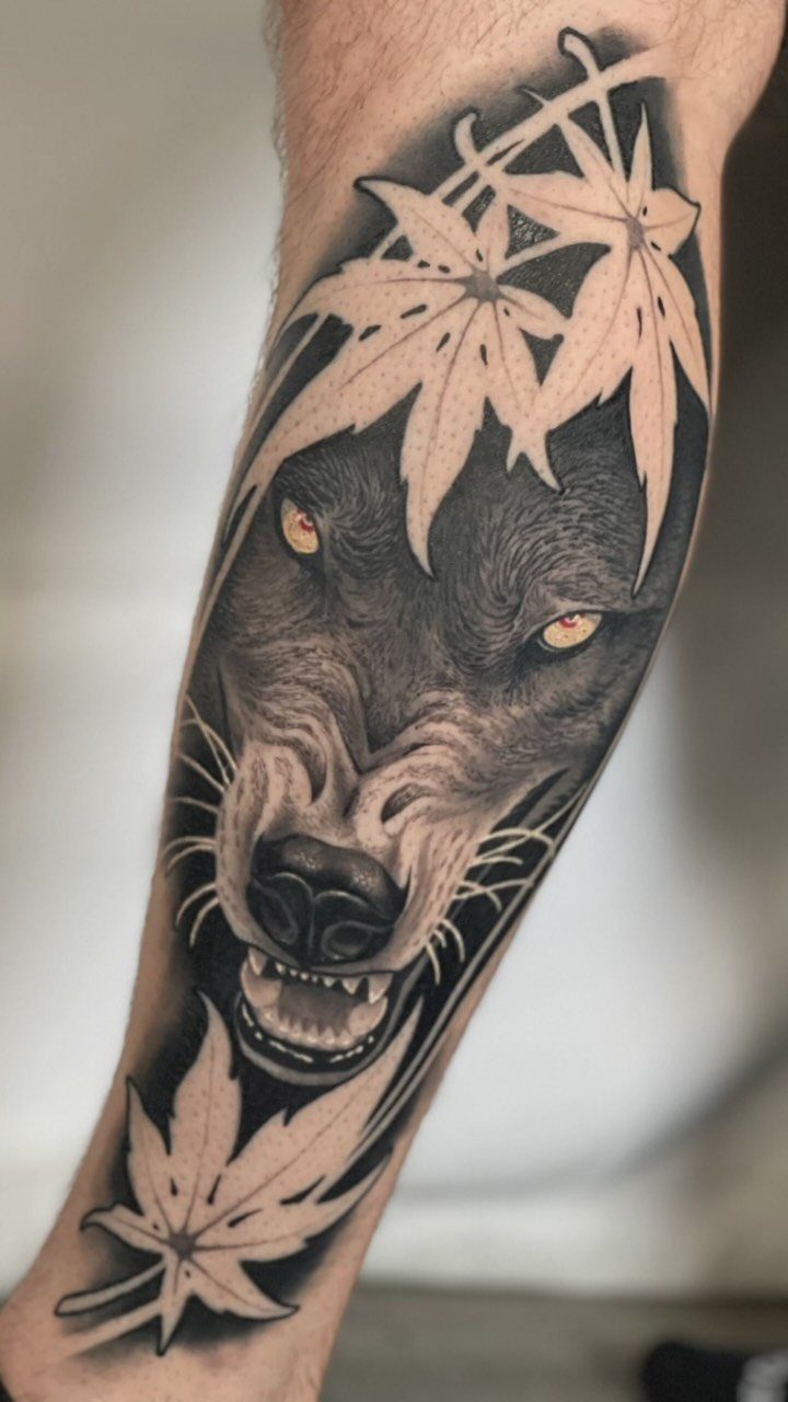 Wolf tattoo on a forearm with yellow eyes and maple leaves