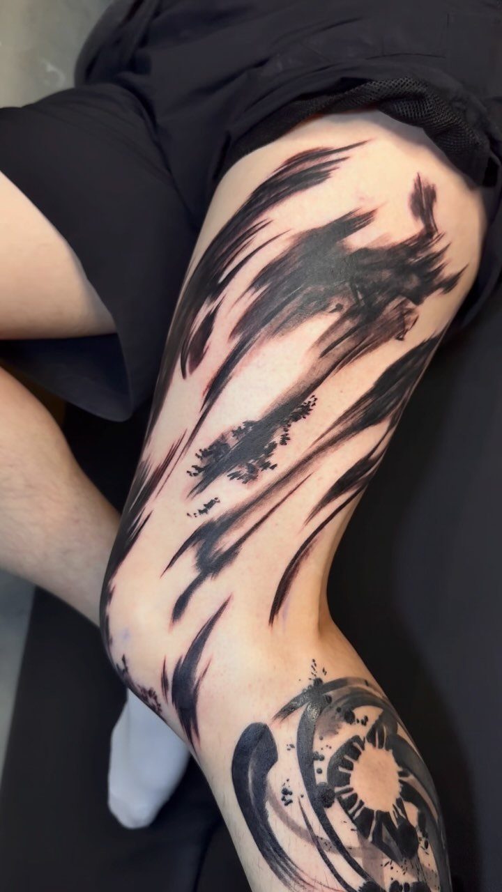 Black ink abstract tattoos with brushstroke patterns on a person's leg