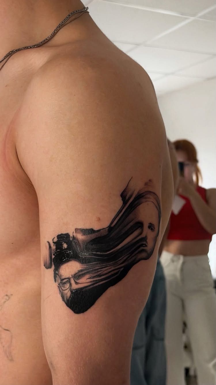Walter White portrait tattoo on a man's upper arm with abstract black ink flows