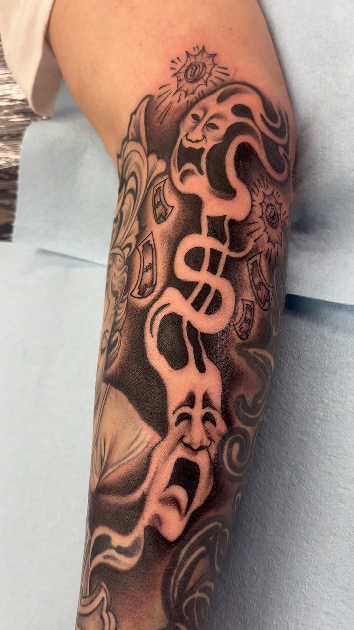 Black and grey tattoo of comedy and tragedy masks with a dollar sign.