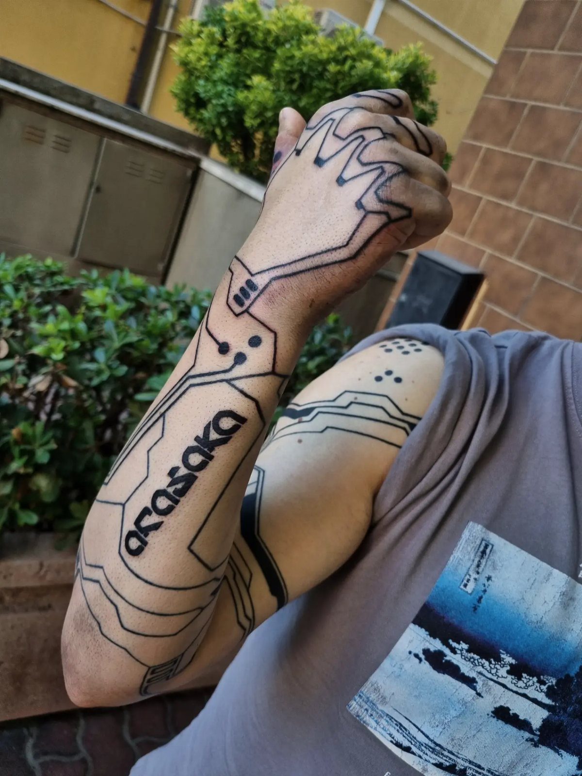 Cyberpunk tattoos with circuit board patterns and Osaka text on a person's arm.