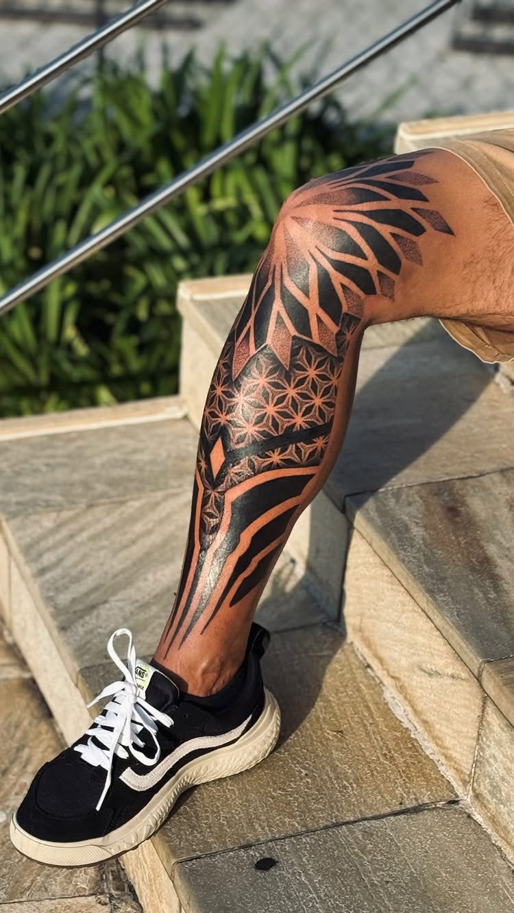 Lower leg and knee with a black geometric mandala tattoo on stone steps.