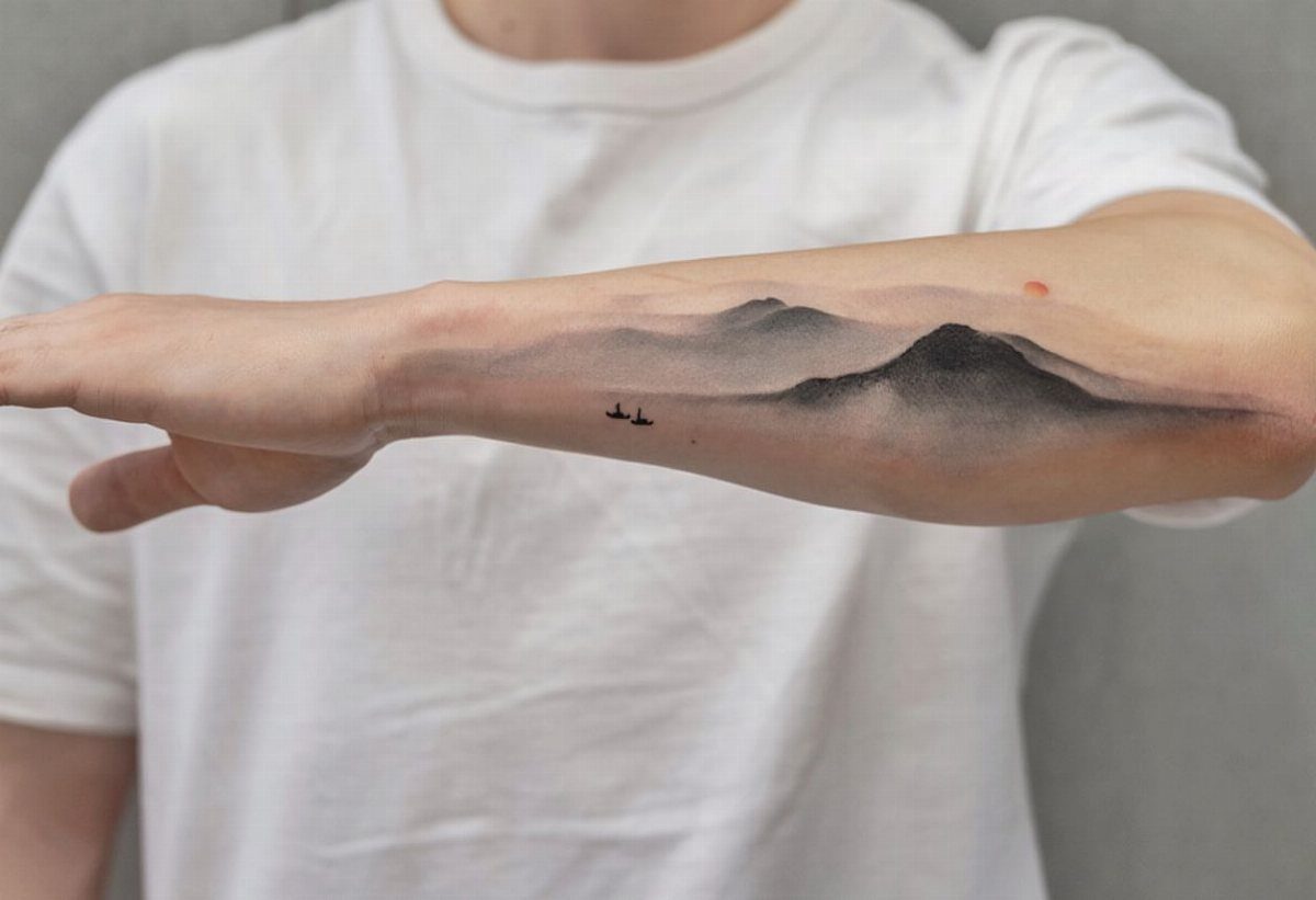 Mountain range tattoo with soft shading and small birds on a person's forearm