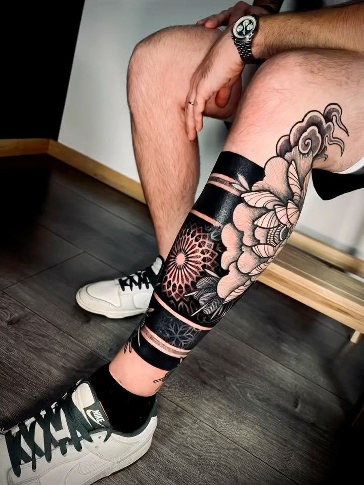 Lower leg tattoo featuring a detailed circular mandala and floral black ink designs.