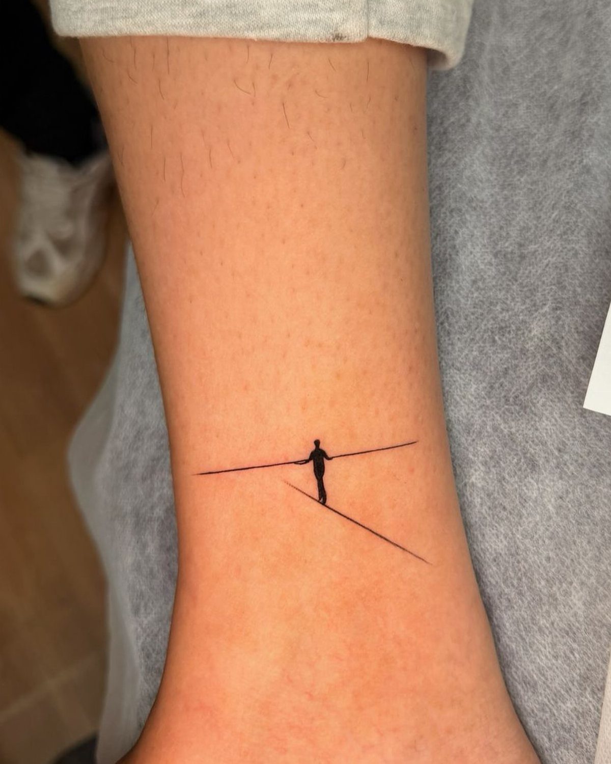 Small black ink tattoo of a tightrope walker silhouette on a person's forearm.