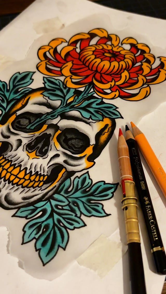 Skull tattoo drawing with teal leaves and an orange chrysanthemum and colored pencils.
