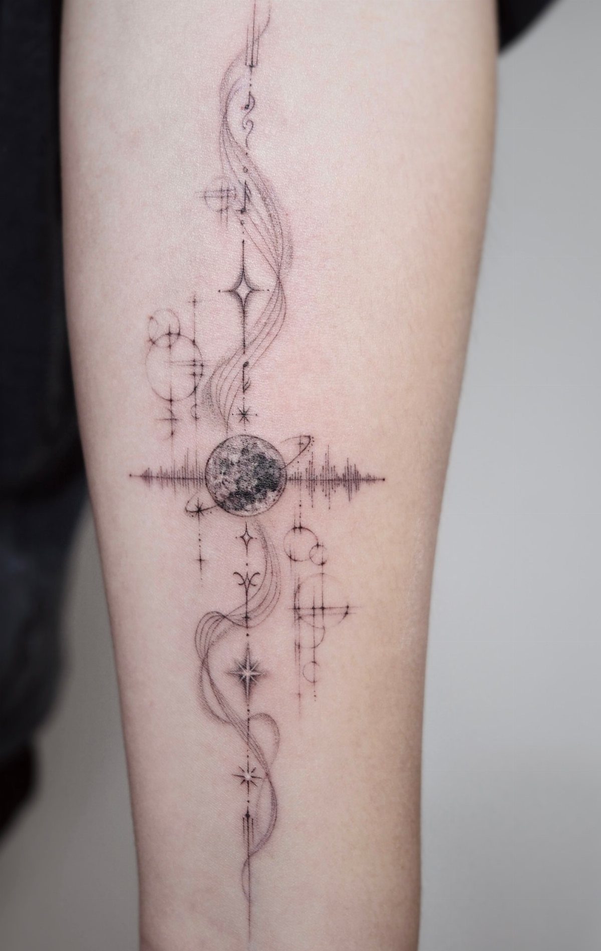 Fine line tattoo of a moon with a sound wave and celestial stars.