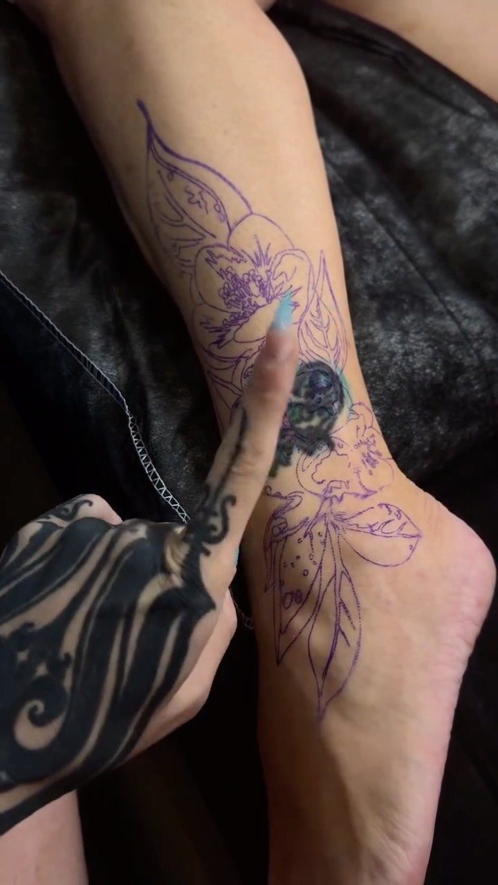 Purple floral tattoo stencil on a lower leg covering an old dark tattoo.
