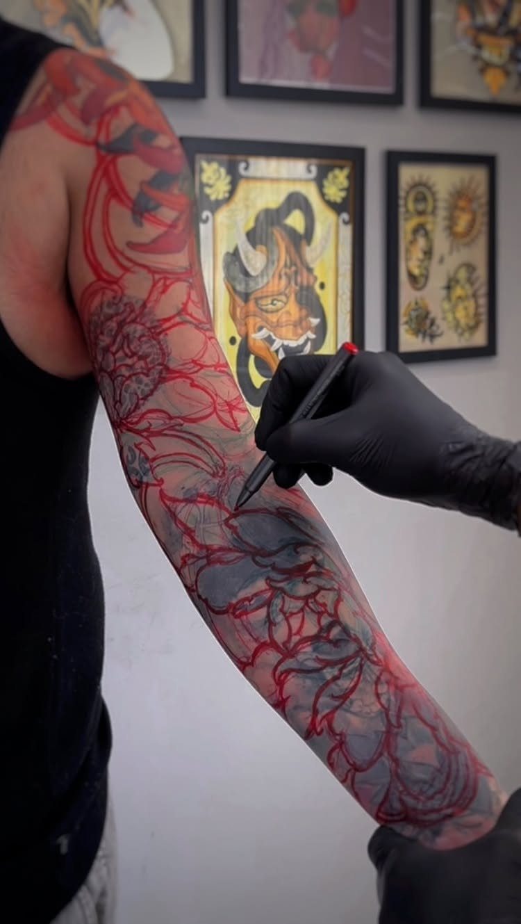 Tattooed arm with red marker outlines being drawn for a cover up design