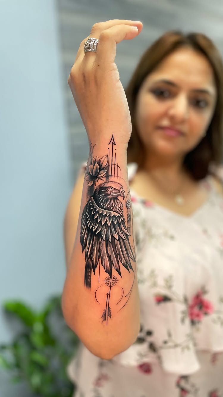 Eagle tattoo with an arrow and flowers on a person's inner forearm and wrist